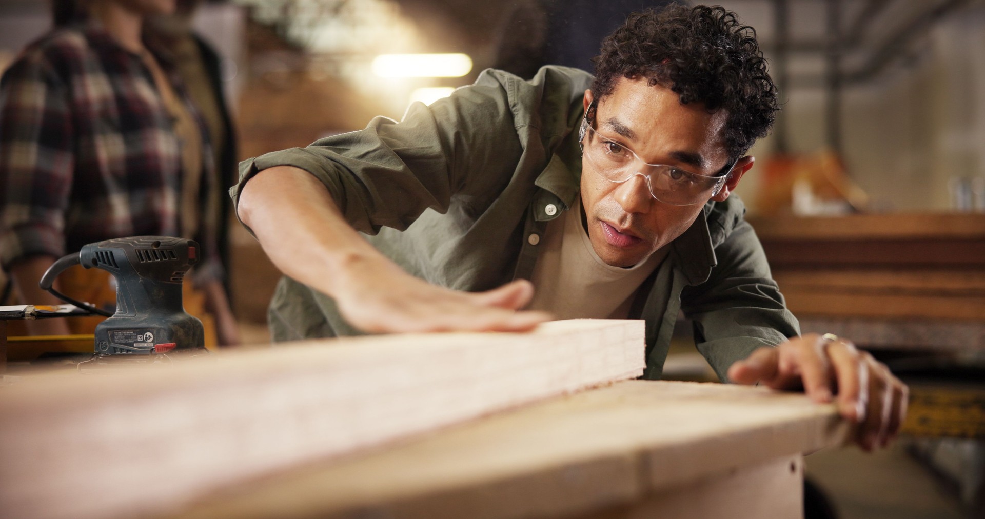 Man, carpenter or wood with smooth finish on workbench for polish, craft or timber project. Male person, woodworker or safety glasses with wooden repair or lumber restoration at workshop or warehouse